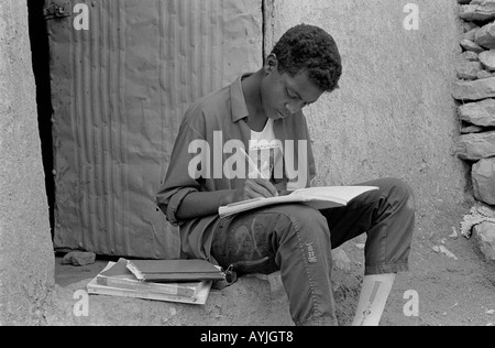 B/W d'un pauvre garçon étudiant avec des livres à la porte.Mekelle, Tigray, Éthiopie, Afrique Banque D'Images