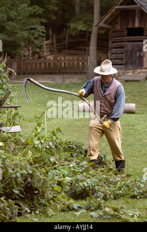 L'homme en costume à l'aide d'une faux pour couper les mauvaises herbes sur les terres agricoles Homeplace Entre Les Lacs Michigan Banque D'Images