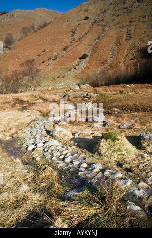 L'autre façon de Cumbria et pierres chemin posé sur zone marécageuse dans Langstrath Valley du soleil donne un éclat doré sur fells Banque D'Images