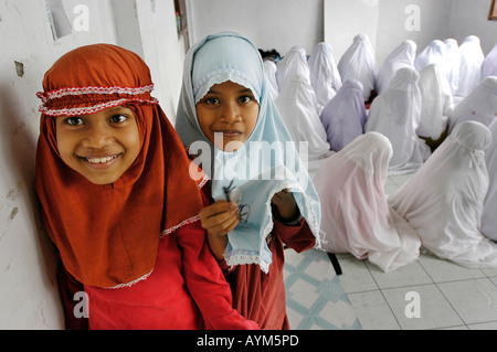 Deux jeunes filles musulmanes à Banda Aceh en Indonésie sont à l'affiche tandis que les filles plus âgées prier Banque D'Images