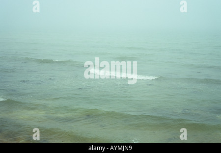 Douces vagues avec un blanc de rupture dans une vue gris-vert d'une mer de brouillard Banque D'Images