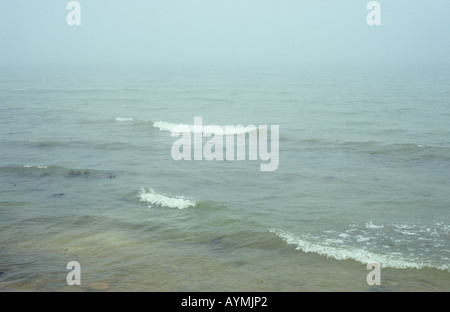 Douces vagues avec trois blancs de rupture dans une vue gris-vert d'une mer de brouillard Banque D'Images