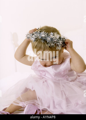 Baby Girl wearing a pink party dress mettant un halo de guirlandes sur la tête. Banque D'Images