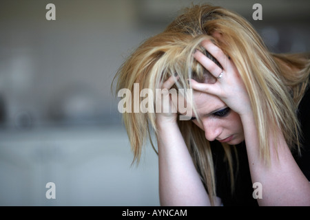 Close up de la tête et les épaules des jeunes adolescents blond femme assise, la tête dans ses mains à la maison dans sa cuisine Banque D'Images