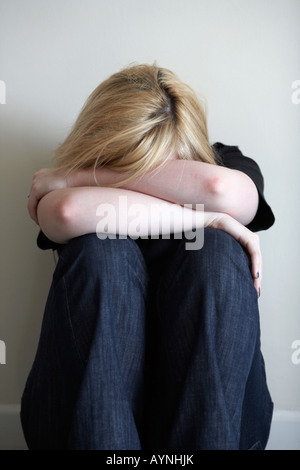 Close up d'armes et les épaules de l'adolescent aux cheveux blonds femme assise en position fœtale sur marbre avec dos au mur Banque D'Images