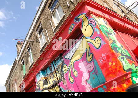 Le Graffiti d'un chien lécher le coin du bâtiment peint sur shop dans Hepscott Road, Hackney Wick, Londres Banque D'Images