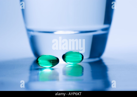 Deux comprimés verts à côté d'un verre d'eau avec une teinte bleue. Banque D'Images