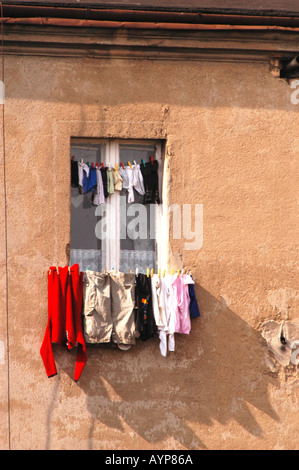 Vieux mur texturé avec une fenêtre et linge suspendu séchant sur les cordes à linge au soleil. Banque D'Images