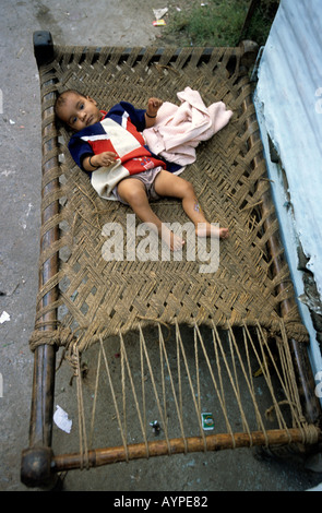 Petite fille hindoue couchée sans surveillance sur un lit de corde primitif en plein air, Delhi, Inde. Banque D'Images