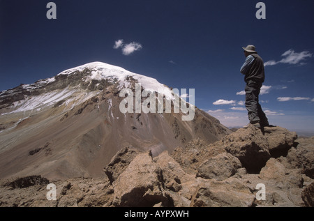 Trekker debout sur des roches volcaniques regardant la vue sur le volcan Sajama, parc national de Sajama, Bolivie Banque D'Images