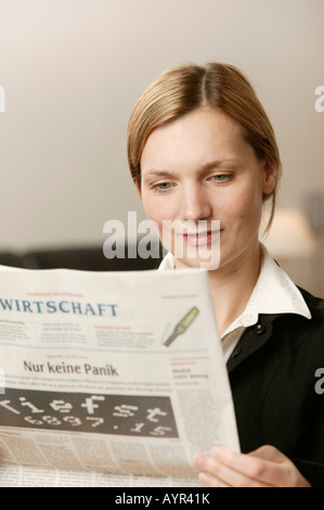 Young blonde woman reading section financière d'un journal, smiling Banque D'Images