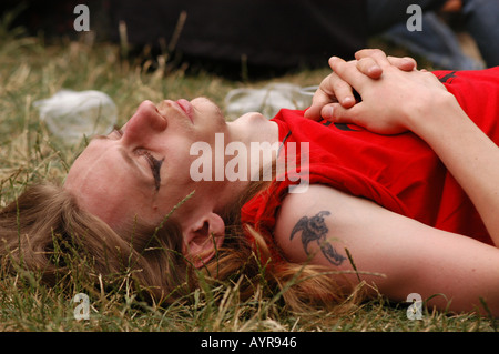Goths pendant Castle Party Music Festival à Bolkow en Pologne, personne couchée sur l'herbe avec les yeux fermés, chemise rouge, tatouage de bras, événement musical en plein air. Banque D'Images