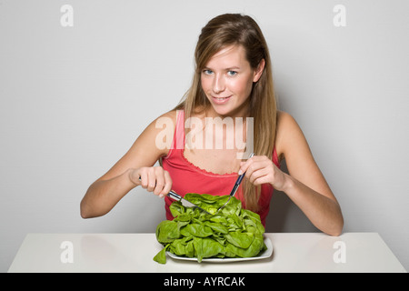 Jeune femme tenant couverts, assiette de salade verte Banque D'Images