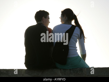 Jeune couple assis sur un mur au coucher du soleil. Banque D'Images