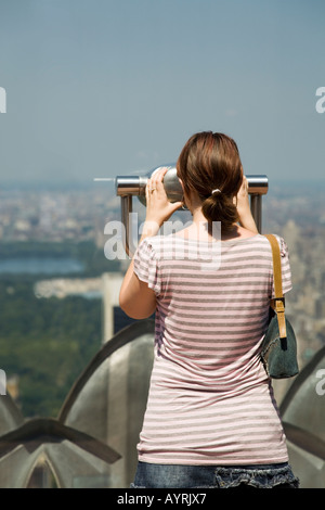 Jeune femme regarde à travers les jumelles sur l'observation de l'étage du Rockefeller Center, New York. Banque D'Images