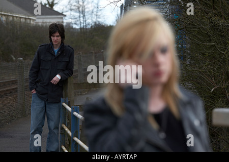 Jeune homme aux cheveux blonds regardant debout femme adolescente sur téléphone mobile pour faire un appel Banque D'Images