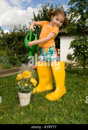 Girl watering son fleurs jaunes portant des bottes en caoutchouc jaune Banque D'Images