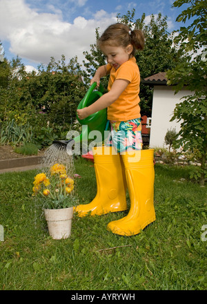 Girl watering son fleurs jaunes portant des bottes en caoutchouc jaune Banque D'Images