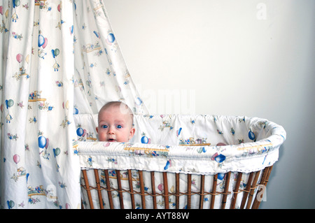 Bébé de quatre mois garçon lorgnant sur le bord de son berceau Banque D'Images