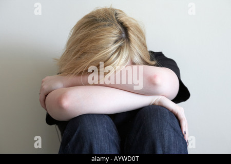 Close up d'armes et les épaules de l'adolescent aux cheveux blonds femme assise en position fœtale sur marbre avec dos au mur Banque D'Images