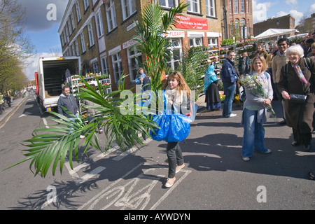 Une jeune femme transportant plusieurs grandes usines à Columbia Road Flower Market à Londres Banque D'Images