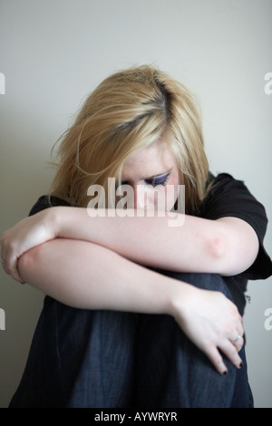 Close up d'armes et les épaules de l'adolescent blond woman sitting on floor avec dos au mur Banque D'Images