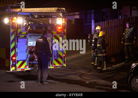 Les pompiers en attente derrière un camion d'incendie moteur de pompage sur la scène de l'incendie d'une maison au Royaume-Uni Banque D'Images