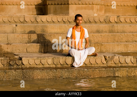 Jeune prêtre indien méditant dans un ghat sur la rive du Gange au lever du soleil à Varanasi, Uttar Pradesh, Inde. Banque D'Images