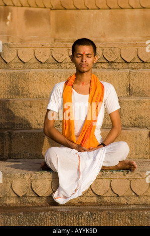 Jeune prêtre indien priant et méditant à un ghat sur la rive du Gange au lever du soleil à Varanasi, Uttar Pradesh, Inde. Banque D'Images