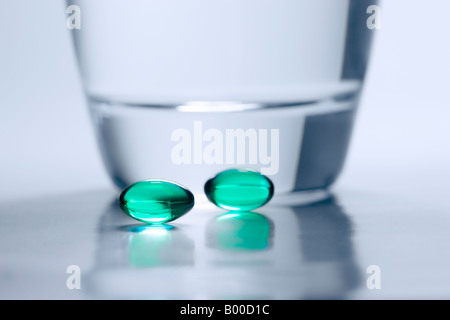 Deux comprimés verts à côté d'un verre d'eau Banque D'Images