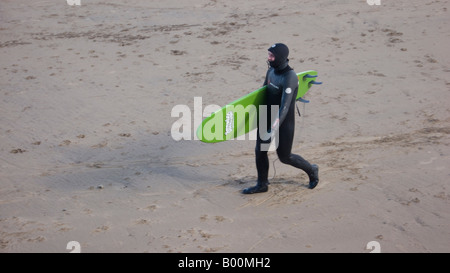 Man wearing wetsuit transportant surfboard on beach Banque D'Images