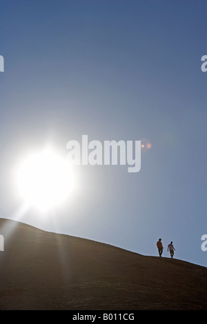 La Namibie, région d'Erongo, Swakopmund. Décrit par le soleil levant, une paire de marcheurs sont décrits comme ils cimier le haut d'une dune. Banque D'Images