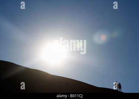 La Namibie, région d'Erongo, Swakopmund. Décrit par le soleil levant, une paire de marcheurs sont décrits comme ils cimier le haut d'une dune. Banque D'Images