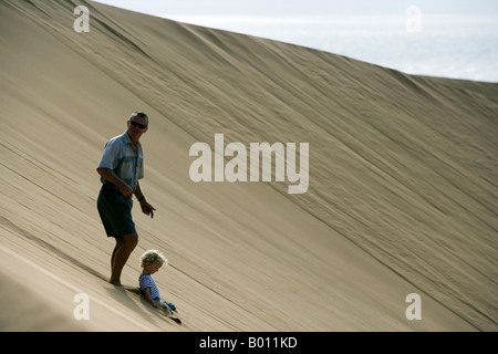 La Namibie, région d'Erongo, Swakopmund. Sur les dunes de sable entre Swakopmund et Walvis Bay une famille glisser le long du côté de la dune Banque D'Images