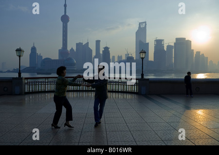 Couple de danses à l'exercice en tant que soleil se lève sur la ville, le Bund, Shanghai, Chine Banque D'Images