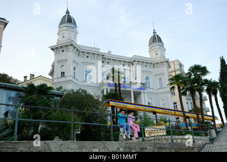 2 enfants portant des bérets français, assis sur main courante, l'amiral bâtiment Casino en arrière-plan. Opatija, Croatie Banque D'Images