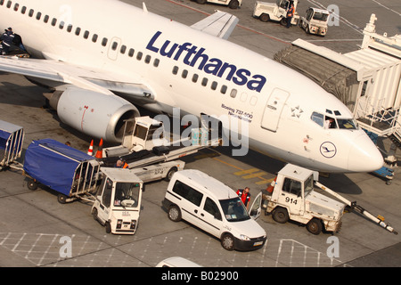 Lufthansa Boeing 737 avion de ligne avion à l'aéroport entouré par les véhicules de service de manutention au sol et des bagages remorqueur Banque D'Images