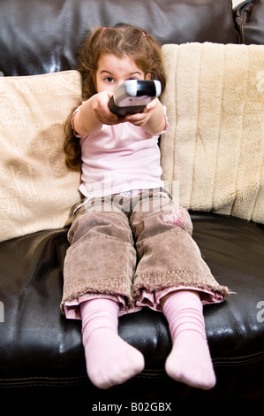 Une jeune fille de 4 ans démontre l'utilisation de la télécommande d'une télévision tout en regardant la télévision Banque D'Images