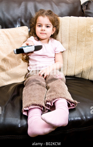 Une jeune fille de 4 ans démontre l'utilisation de la télécommande d'une télévision tout en regardant la télévision Banque D'Images