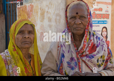 Deux personnes âgées fier dans shawled matrones indiennes saris en face d'un contemporain de l'affiche. Banque D'Images