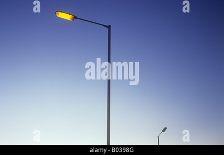 Grand lampadaire élancé contre orange éclatant début de soirée mauve ciel avec lampe lointain pas encore allumé Banque D'Images