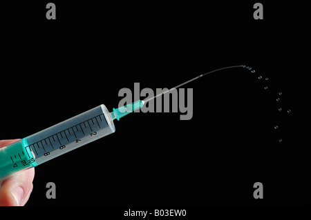 Main tenant une seringue sur un fond noir Banque D'Images