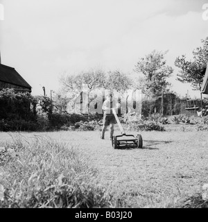 OLD VINTAGE SNAPSHOT FAMILLE PHOTOGRAPHIE DE JEUNE GARÇON POUSSANT VIEILLE TONDEUSE DANS LE JARDIN Banque D'Images