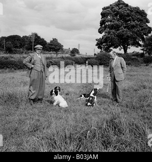 OLD VINTAGE SNAPSHOT FAMILLE PHOTO DE DEUX HOMMES PORTANT DES VÊTEMENTS EN PAYS TWEED CHAMP AVEC DEUX CHIENS Banque D'Images