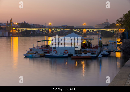 Puente de Isabel II, de l'autre côté de Rio Guadalquivir (rivière) à Triana avec une jetée et restaurant au premier plan au crépuscule Banque D'Images