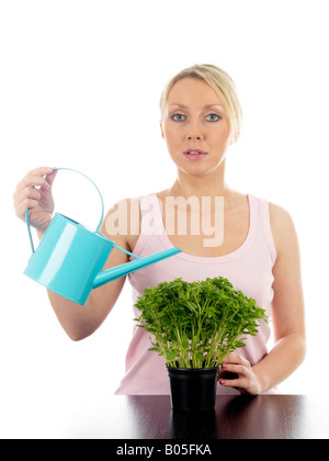 Jeune femme d'arroser un pot de fines herbes prêts à prendre et faire cuire avec un bidon isolé sur un fond blanc et Clipping Path Banque D'Images