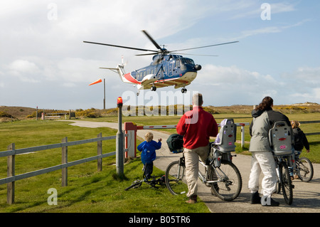 Famille sur les bicyclettes, affichage hélicoptère décollant de l'héliport de Tresco, l'île de Scilly. Banque D'Images