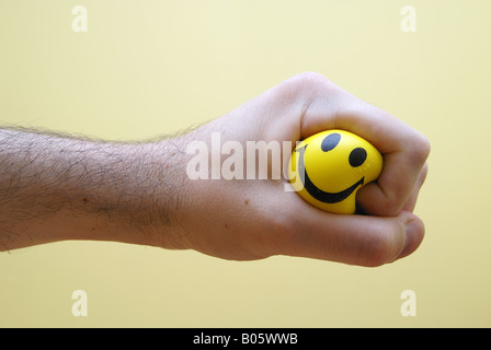 Une serre la main une balle anti-stress en caoutchouc. Un visage heureux imprimé sur la balle peut être vu entre les doigts de la main. Banque D'Images