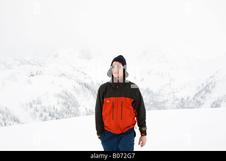 Un jeune homme marche dans la neige, avec des montagnes en arrière-plan pâle au mont Baker, Washington. Banque D'Images