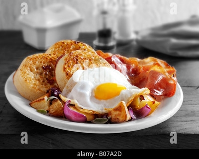 Le petit déjeuner anglais complet avec des crumpets, servi sur une plaque blanche dans une table - œuf frit, bacon, pommes sautées et les crumpets Banque D'Images